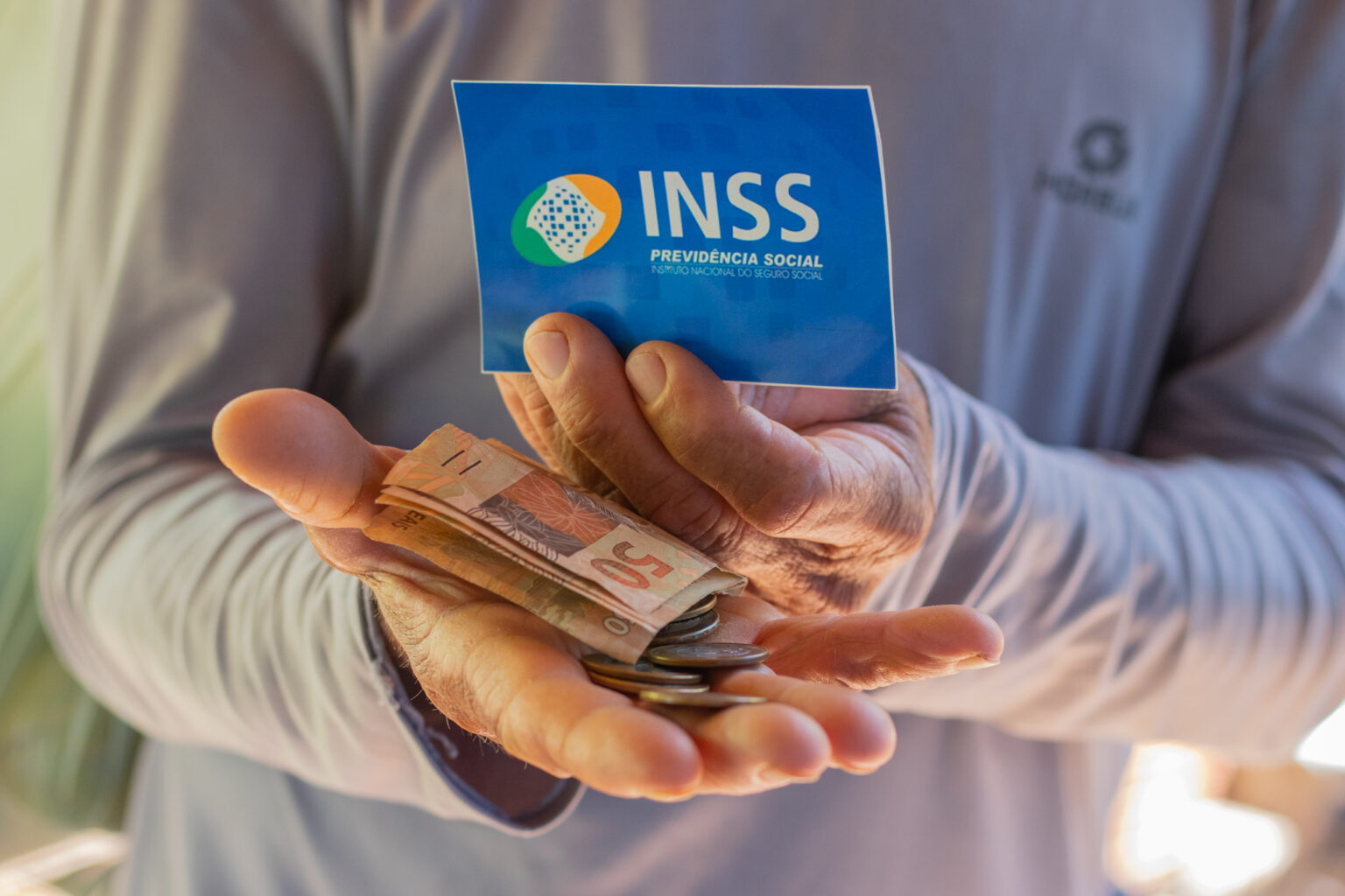 Pessoa idosa segura cartão do INSS e dinheiro em espécie, simbolizando o recebimento de valores retroativos de benefícios previdenciários.
