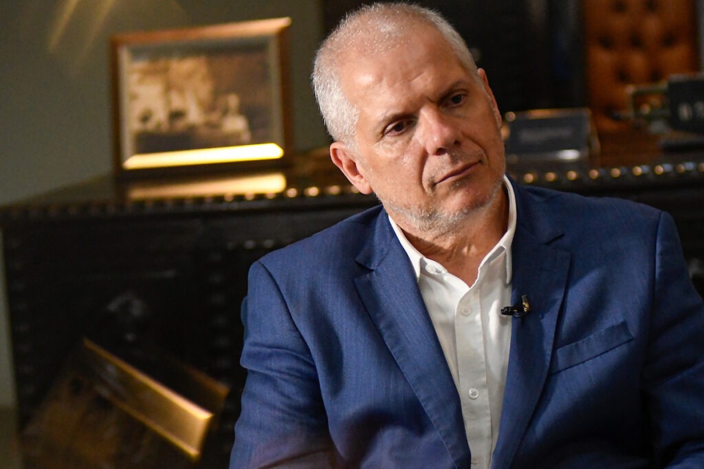 A Polícia Federal prendeu Alessandro Stefanutto Homem de terno azul sentado em ambiente interno, olhando para o lado durante entrevista.