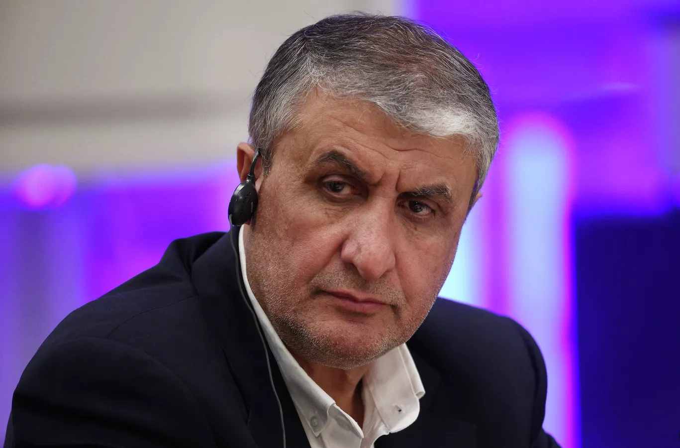 Autoridade iraniana de cabelos grisalhos usa fone de ouvido durante evento oficial, olhando para o lado com expressão séria.