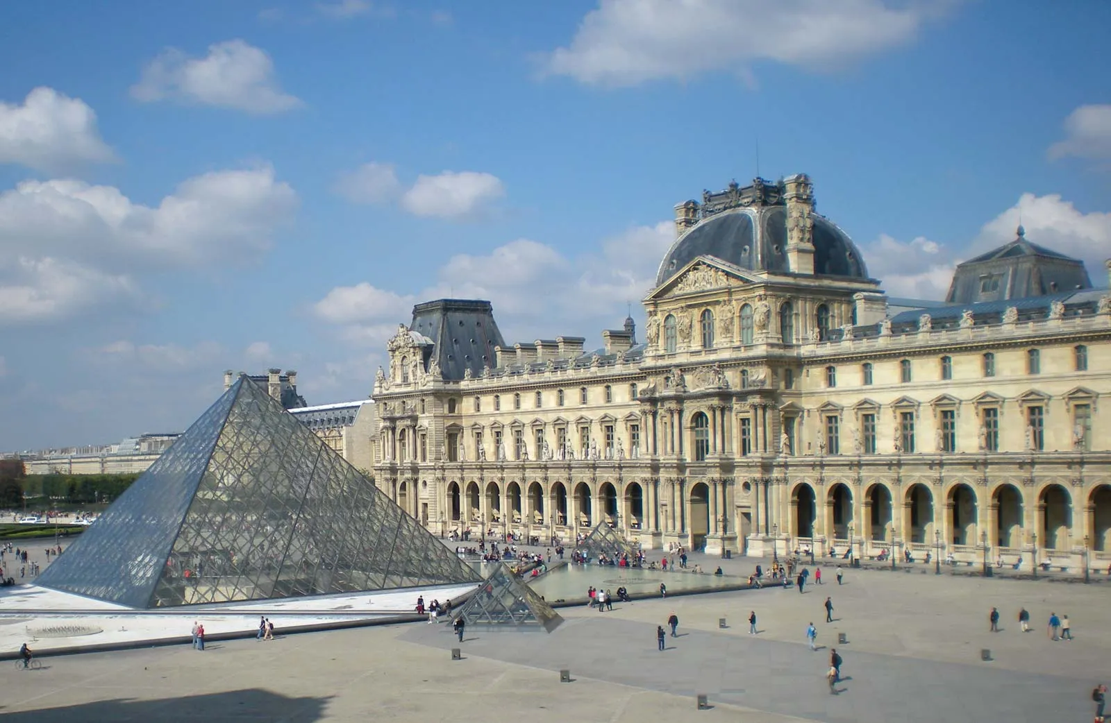 Vista externa do Museu do Louvre em Paris com pirâmide de vidro e edifício histórico sob céu azul