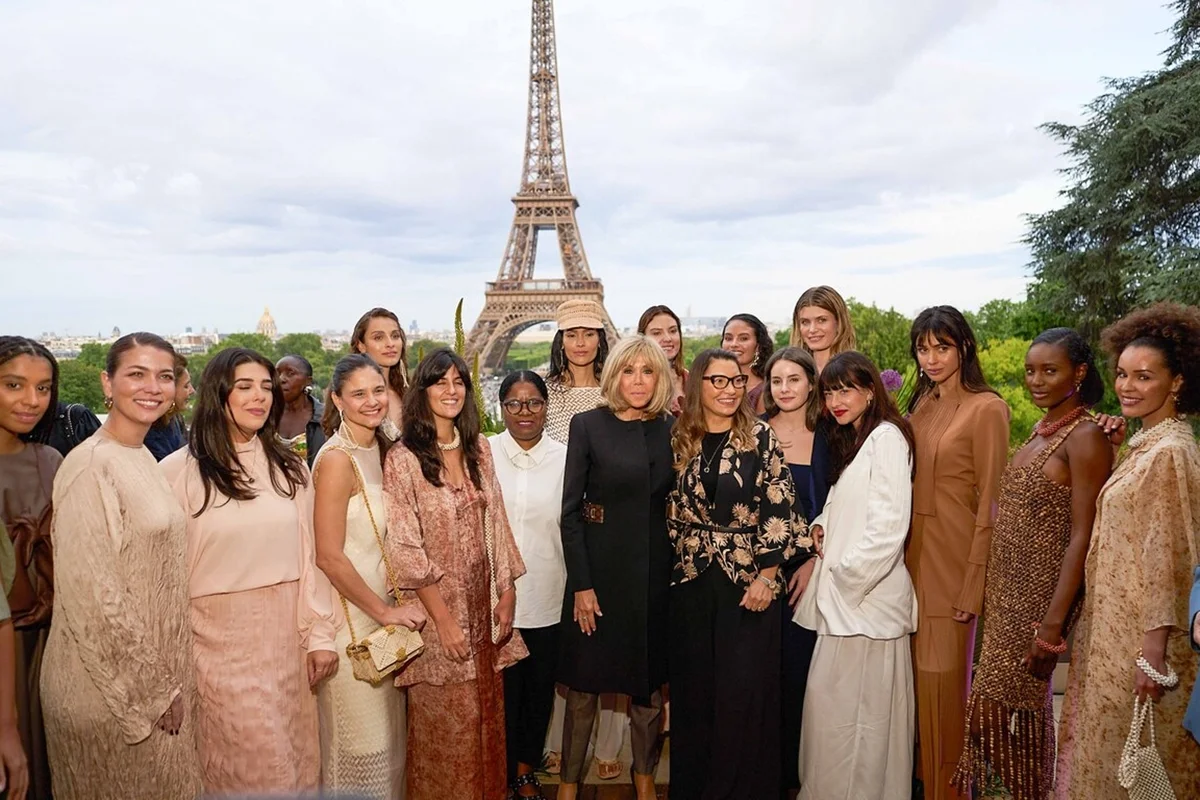 Grupo de mulheres posando diante da Torre Eiffel durante evento oficial em Paris, com Brigitte Macron ao centro da imagem.