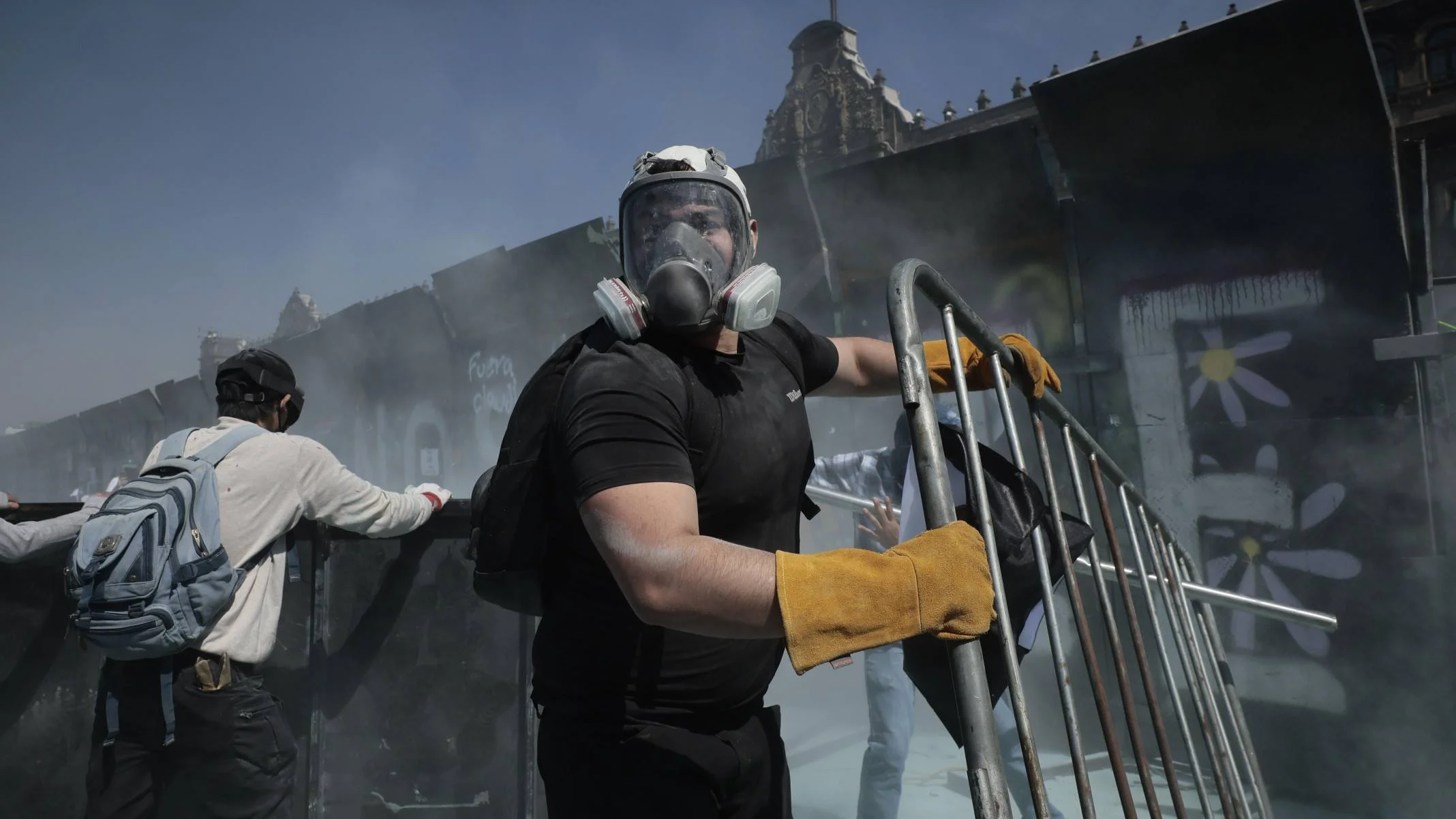 Manifestantes usando máscaras e equipamentos de proteção removem barricadas diante de forte presença de fumaça próximo ao Palácio Nacional, no México.
