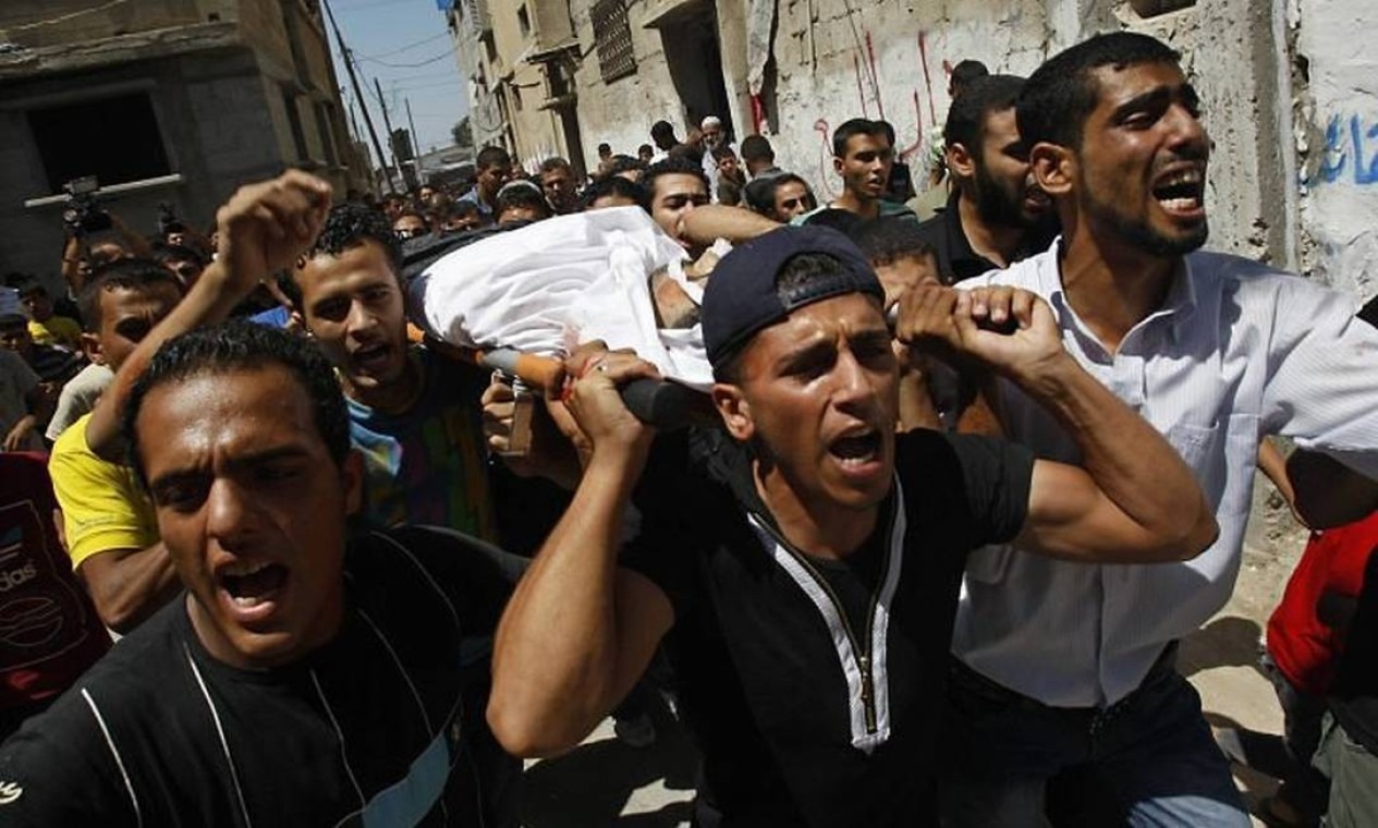 Homens palestinos carregam o corpo de um homem envolto em tecido branco durante cortejo fúnebre nas ruas de Rafah, após confronto na região.