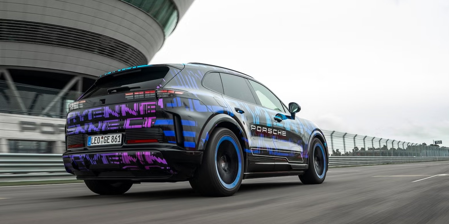 SUV elétrico da Porsche em teste de pista, visto por trás, com camuflagem colorida e rodas de aro azul em alta velocidade.