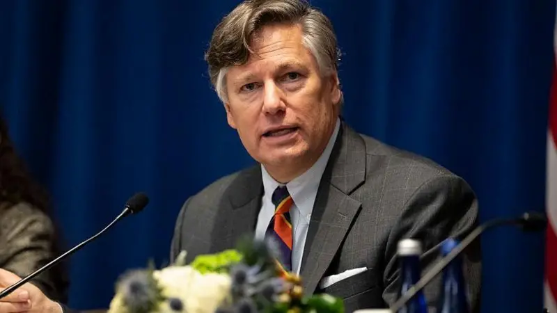 : Christopher Landau, vice-secretário de Estado dos EUA, discursa em evento oficial com microfone e bandeira americana ao fundo