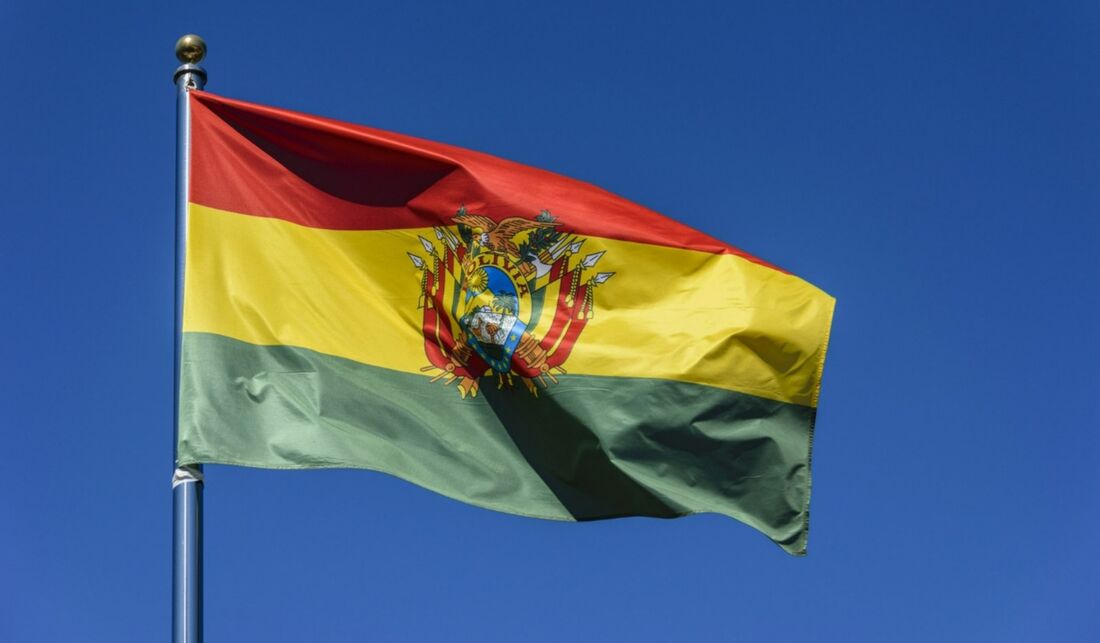 Bandeira da Bolívia tremulando ao vento, com as cores vermelho, amarelo e verde contra um céu azul.