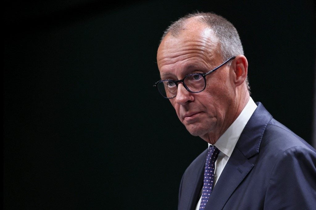 Chanceler alemão em close, usando óculos e terno escuro, olhando de lado em ambiente fechado.