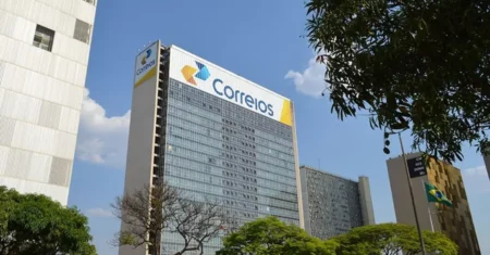 Prédio-sede dos Correios visto de baixo, com logotipo em destaque na fachada e árvores ao redor.