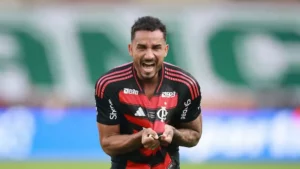 Jogador Danilo do Flamengo grita de euforia segurando o escudo da camisa com as duas mãos em campo após marcar gol.