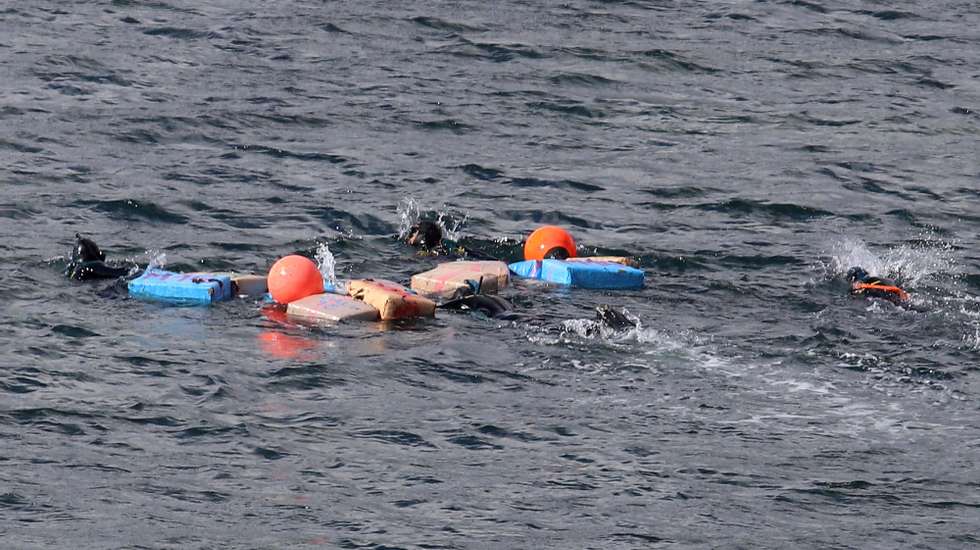 Pessoas nadando com coletes salva-vidas laranja e azuis em águas escuras do oceano