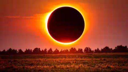 Eclipse mais longo do século transformará dia em noite em 2027 Eclipse solar total mostrando disco negro da Lua completamente cobrindo o Sol com coroa solar dourada brilhante visível ao redor, sobre paisagem de campo com vegetação alaranjada e linha de árvores no horizonte sob céu avermelhado