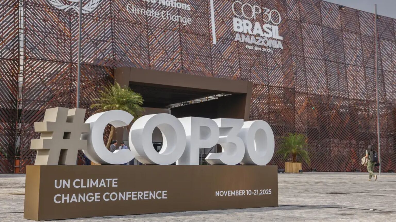 Entrada principal da COP30 com estrutura metálica decorativa ao fundo e letreiro gigante “#COP30” exposto na área externa do evento.