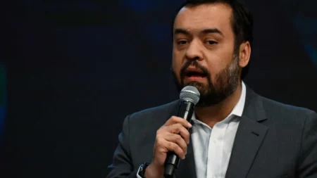 Autoridade do governo do Rio de Janeiro discursa segurando microfone em evento oficial com fundo escuro