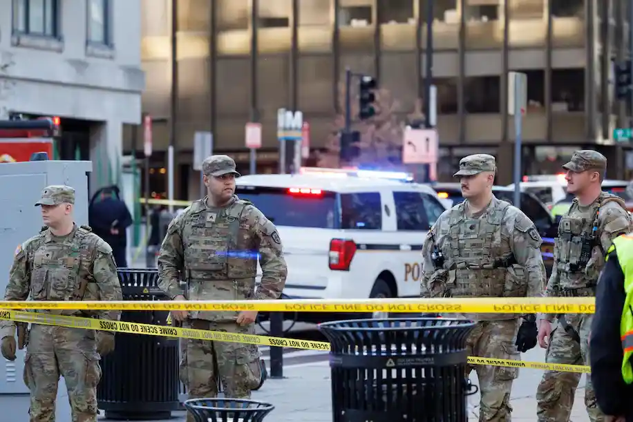 Militares da Guarda Nacional em uniforme camuflado na cena do tiroteio próximo à estação Farragut West em Washington, com fita de isolamento policial e viaturas ao fundo