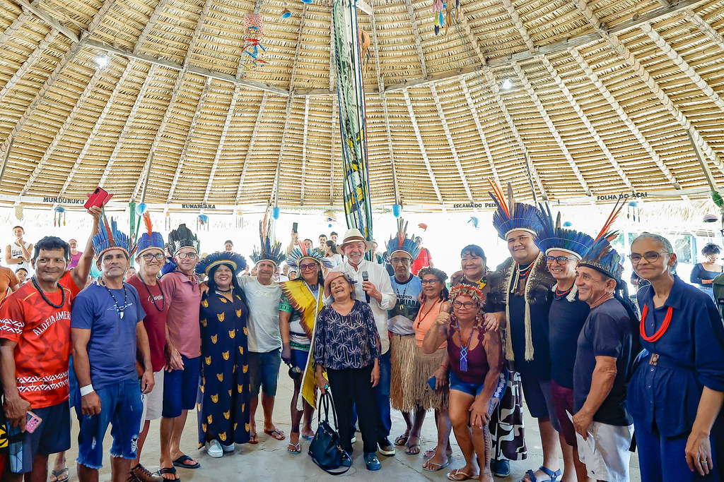 Presidente participa de visita à aldeia Kumaruara, em espaço cultural indígena, cercado por lideranças locais com cocares e trajes tradicionais.