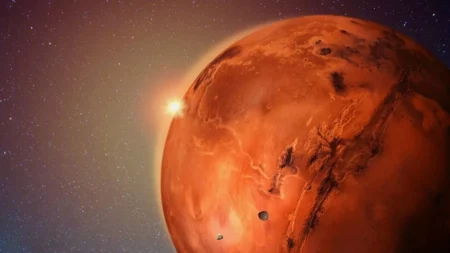 Planeta Marte visto de perto, com superfície avermelhada, crateras visíveis e o sol brilhando ao fundo no espaço.