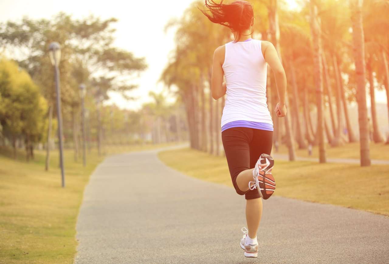 Mulher pratica corrida em parque ao ar livre durante o pôr do sol, simbolizando os benefícios do exercício físico para o bem-estar mental.