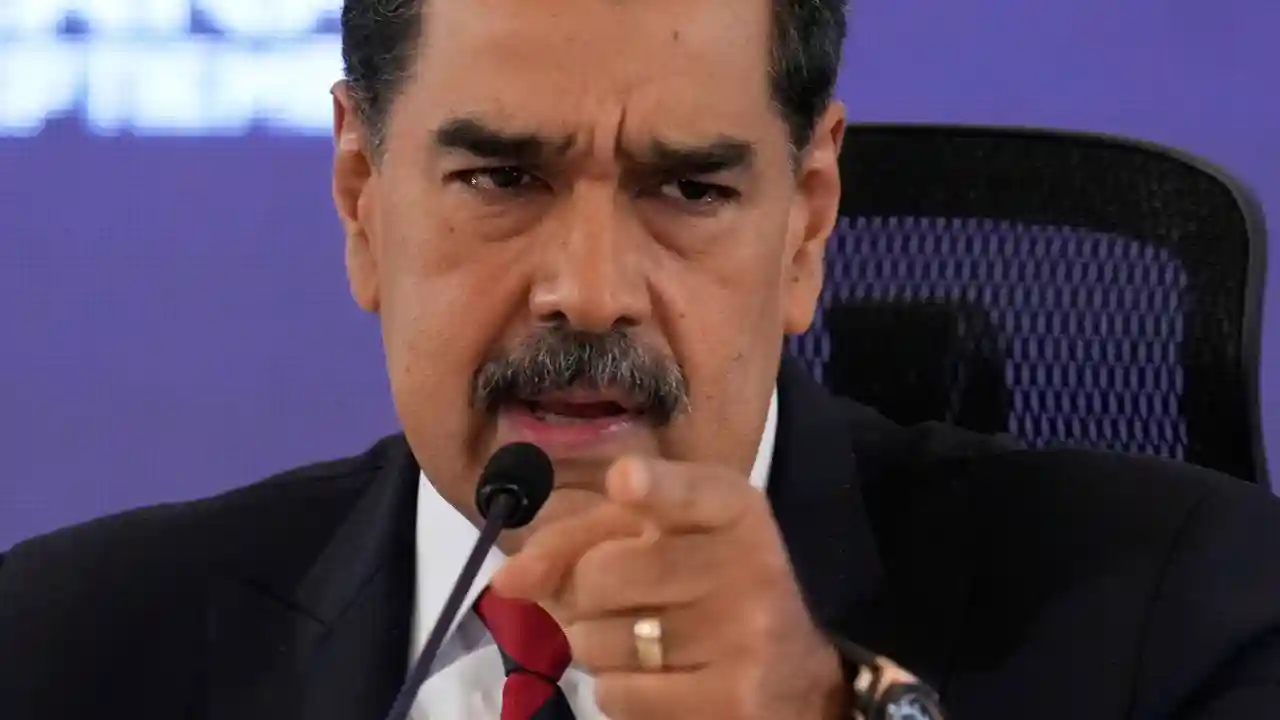 Presidente venezuelano Nicolás Maduro em coletiva de imprensa gesticulando com o dedo indicador apontado para frente, vestindo terno preto e gravata vermelha, com expressão séria diante de microfone