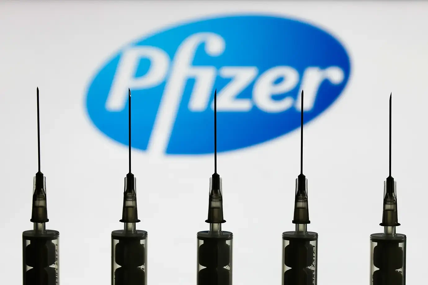 Seringas alinhadas diante do logotipo da Pfizer, simbolizando novas vacinas aprovadas pela FDA com aplicação restrita a grupos de risco.