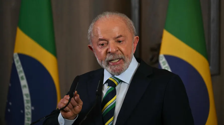 Presidente Lula falando diante de microfones, com duas bandeiras ao fundo.