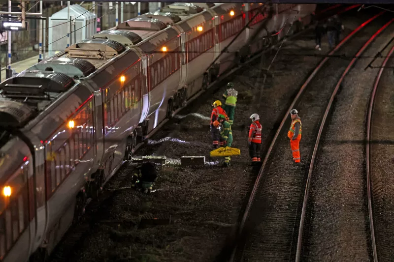 Equipes de emergência trabalham ao lado de trem parado em estação ferroviária durante a noite na Inglaterra