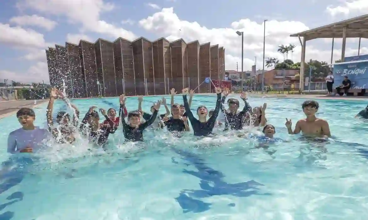 Crianças brincando e comemorando em piscina da Usina da Paz do Bengui no Pará, com estrutura arquitetônica moderna ao fundo sob céu ensolarado