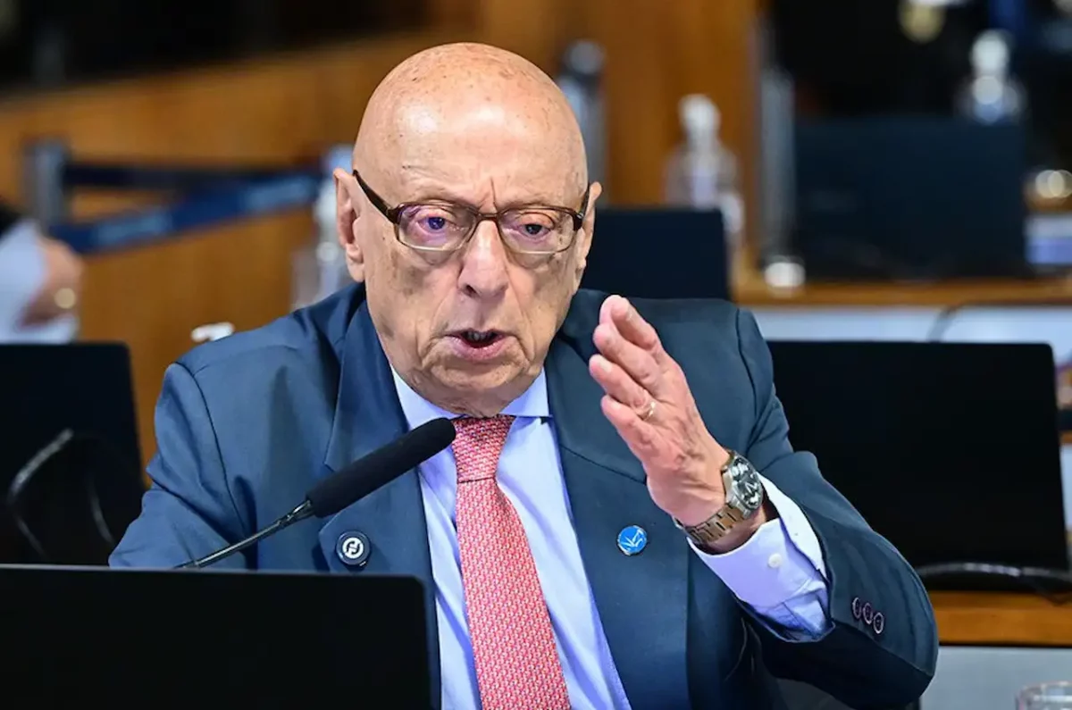 O senador Esperidião Amin, um homem idoso e calvo usando óculos, terno azul-escuro e gravata vermelha, gesticula com a mão esquerda enquanto fala enfaticamente ao microfone durante uma sessão legislativa.