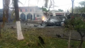 Veículo em chamas e escombros espalhados em frente a um prédio danificado após explosão de carro-bomba em Coahuayana, México.