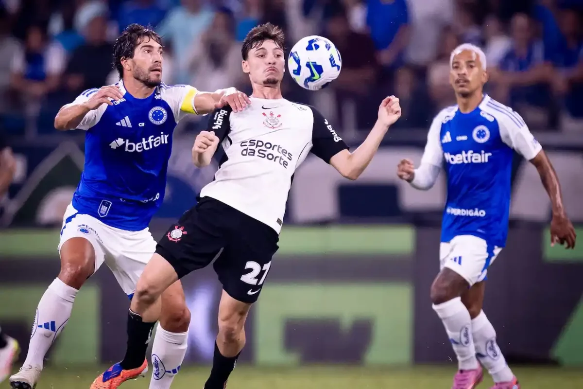 Jogador do Corinthians disputa a bola com atleta do Cruzeiro durante partida, com forte marcação e intensidade, enquanto outro jogador cruzeirense acompanha a jogada ao fundo.