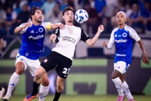 Jogador do Corinthians disputa a bola com atleta do Cruzeiro durante partida, com forte marcação e intensidade, enquanto outro jogador cruzeirense acompanha a jogada ao fundo.