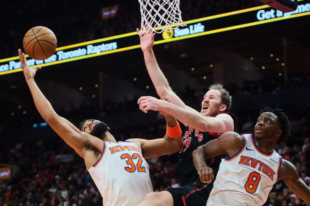 Jogadores de basquete de New York Knicks e Toronto Raptors disputam a bola em partida da NBA Cup.