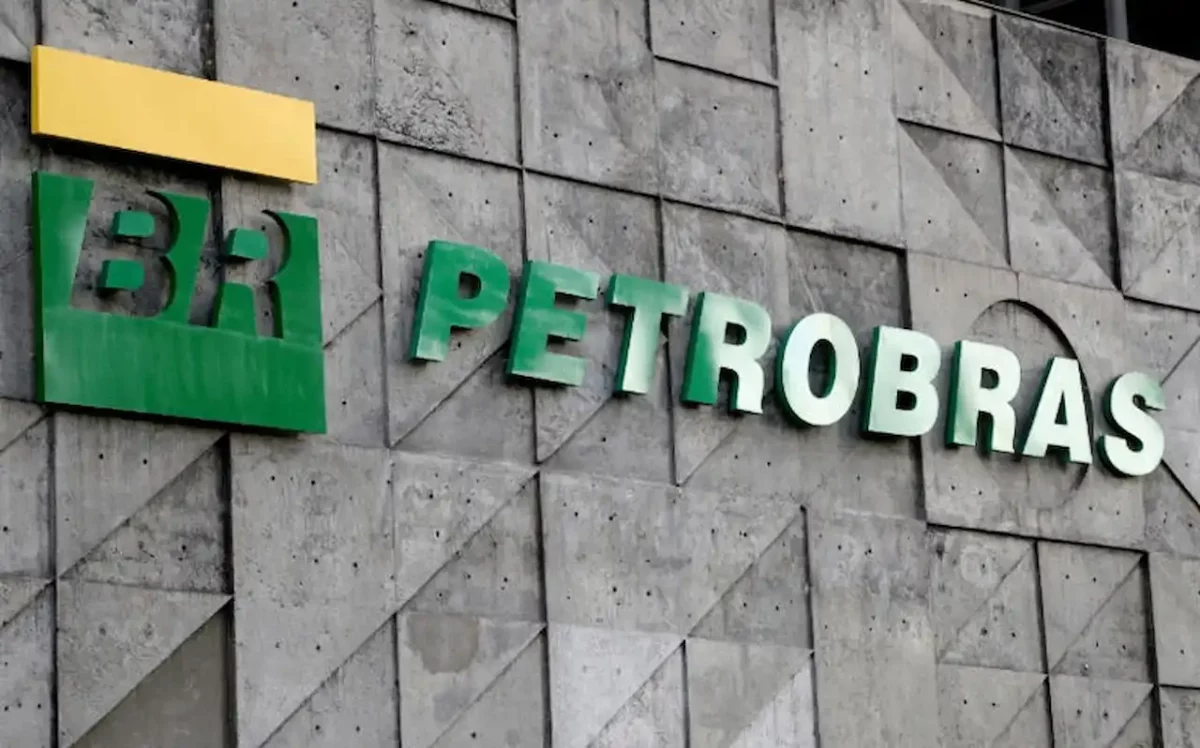 Fachada da sede da Petrobras exibindo o logotipo "BR" em verde e amarelo e o nome da empresa em letras verdes volumétricas, fixadas sobre uma parede de concreto cinza com padrões geométricos em relevo.