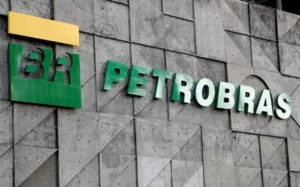 Fachada da sede da Petrobras exibindo o logotipo "BR" em verde e amarelo e o nome da empresa em letras verdes volumétricas, fixadas sobre uma parede de concreto cinza com padrões geométricos em relevo.
