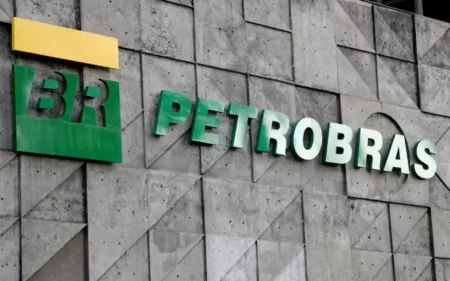 Fachada da sede da Petrobras exibindo o logotipo "BR" em verde e amarelo e o nome da empresa em letras verdes volumétricas, fixadas sobre uma parede de concreto cinza com padrões geométricos em relevo.