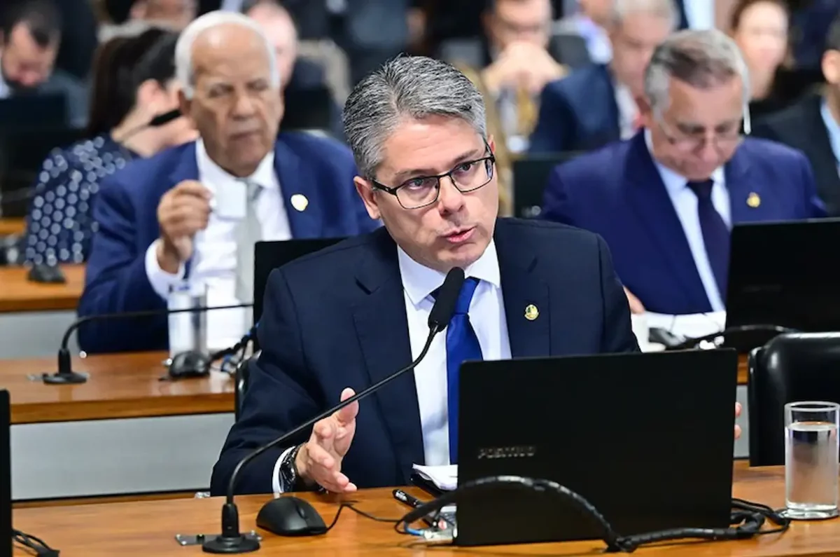 O senador Alessandro Vieira, um homem de pele clara, cabelos grisalhos e usando óculos, fala enfaticamente ao microfone durante uma sessão legislativa; ele veste terno azul-escuro e gravata azul royal, com outros parlamentares desfocados ao fundo.