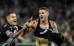 O atacante Pablo Vegetti, sem camisa e com expressão de grito eufórico, é abraçado pelo meia Philippe Coutinho durante a comemoração vibrante do gol da vitória do Vasco em jogo noturno.